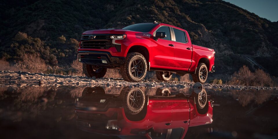 Reflejo de Chevrolet Silverado roja sobre un charco de agua en un camino de tierra.