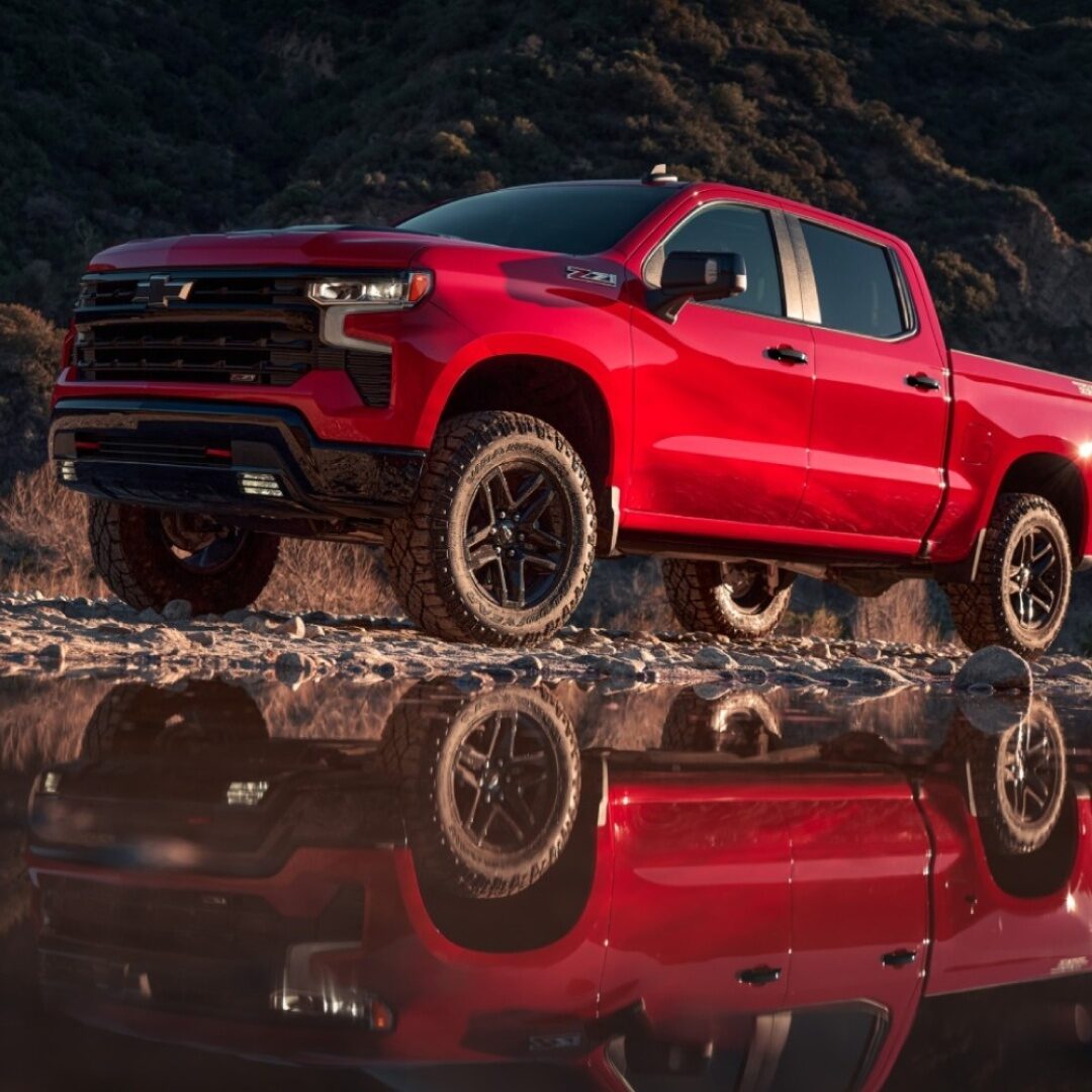 Reflejo de Chevrolet Silverado roja sobre un charco de agua en un camino de tierra.