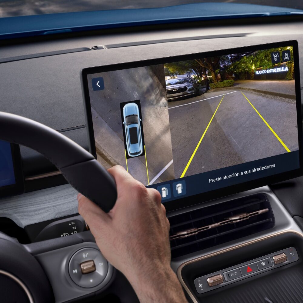 Imagen desde el punto de vista del conductor mientras observa la pantalla central digital y estaciona con la asistencia de la cámara trasera.