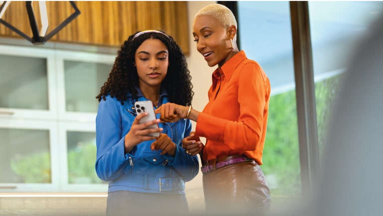 Imagen de una mujer enseñándole a una joven cómo utilizar los comandos remotos de la app myChevrolet desde su smartphone.