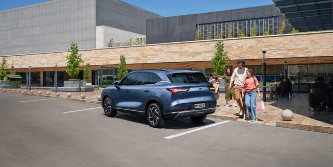 Chevrolet Captiva PHEV estacionada en la puerta de un local comercial mientras una familia se aproxima a ella para guardar bolsas de compras.