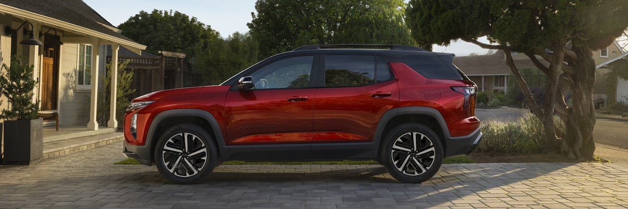 Equinox RS visto de perfil, estacionado em entrada residencial pavimentada, com casas e árvores ao fundo sob luz suave de fim de tarde.