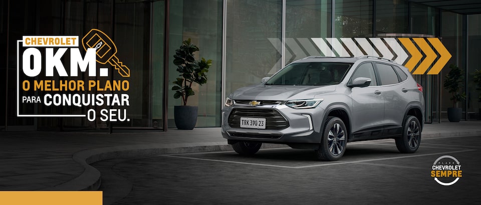 Imagem do SUV Chevrolet Tracker, na cor prata, estacionado em vaga na rua. Arte incentivando a conquista do seu novo zero quilômetro.