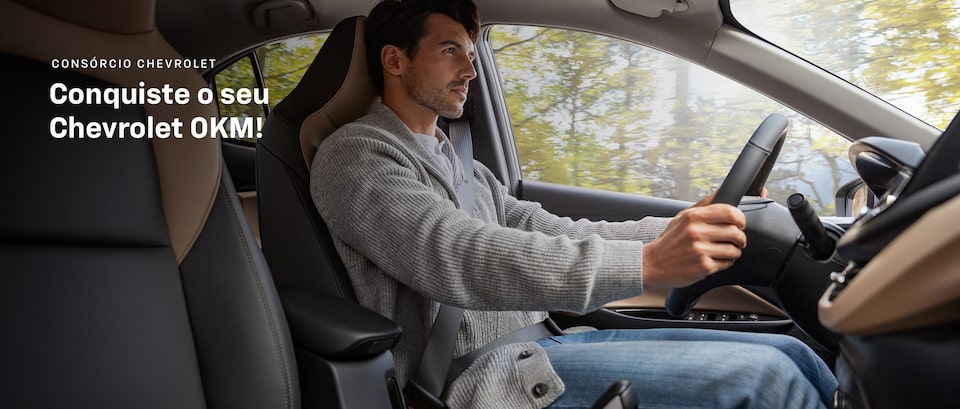 Imagem mostrando um homem branco, jovem, dentro de um Chevrolet, com as mãos no volante. Arte incentivando a conquista do seu novo zero quilômetro.