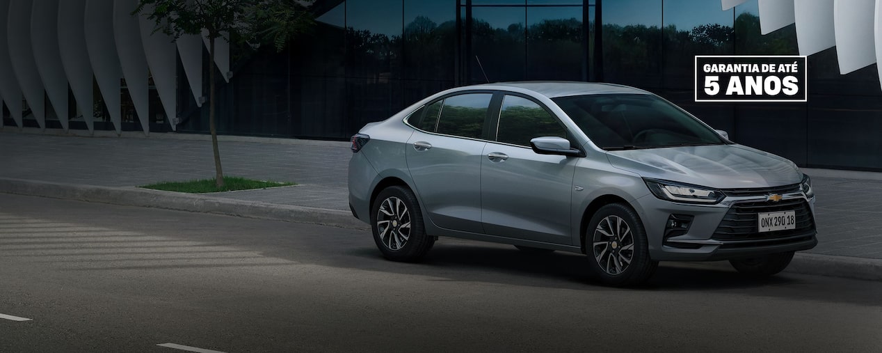  Chevrolet Onix Plus prata estacionado em uma rua de paralelepípedos, com fachada urbana ao fundo.