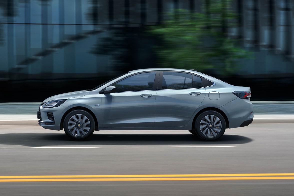 Chevrolet Onix Plus em movimento na cor Prata Shark, com fundo urbano desfocado.