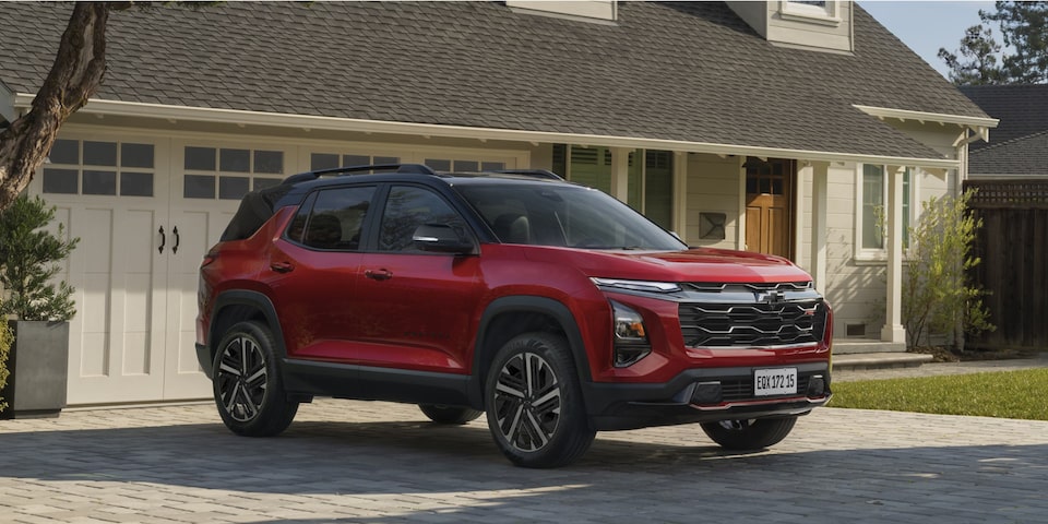 Equinox RS visto de frente e lateral esquerda, estacionado em entrada residencial pavimentada, com garagem e jardim ao fundo sob luz natural.