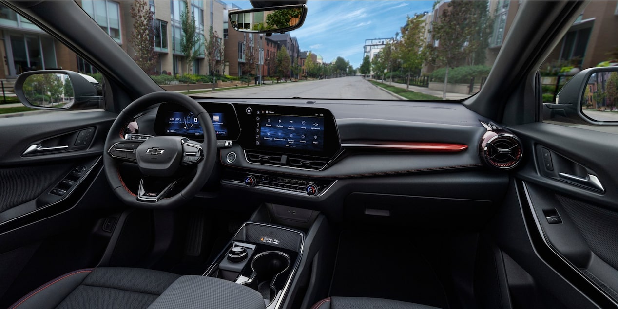 Interior do Chevrolet Equinox visto do banco do motorista, com painel digital, central multimídia ligada e detalhes em acabamento vermelho, estacionado em rua residencial.