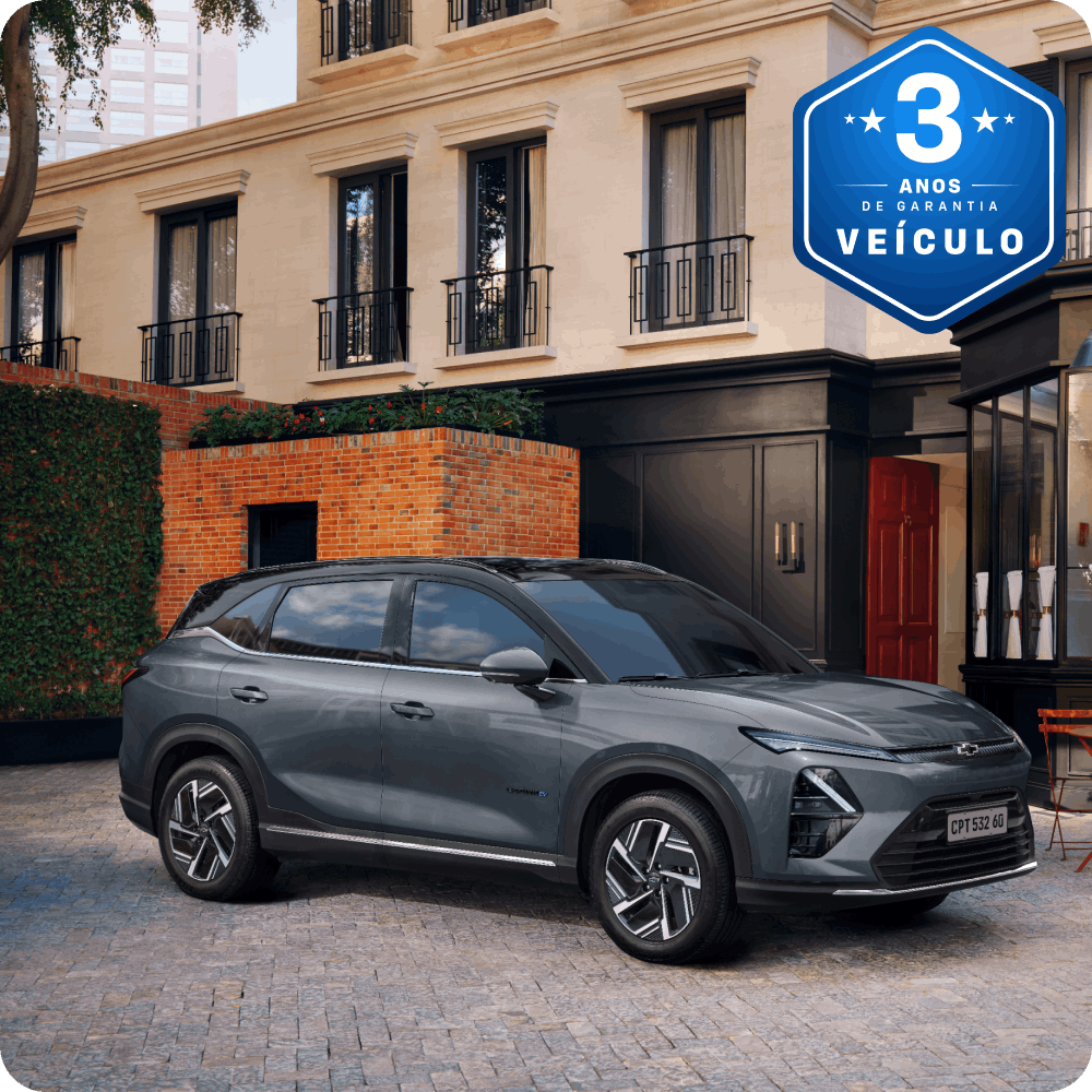 Imagem de um Captiva EV estacionado em frente a um café com mesas externas, em uma rua de paralelepípedos cercada por prédios elegantes com um selo azul indicando 3 anos de garantia do veículo.