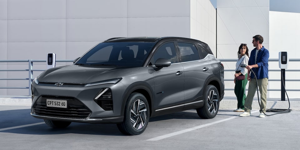 Casal ao lado de um SUV Chevrolet Captiva EV cinza estacionado em um ponto de recarga elétrica em área aberta e moderna.