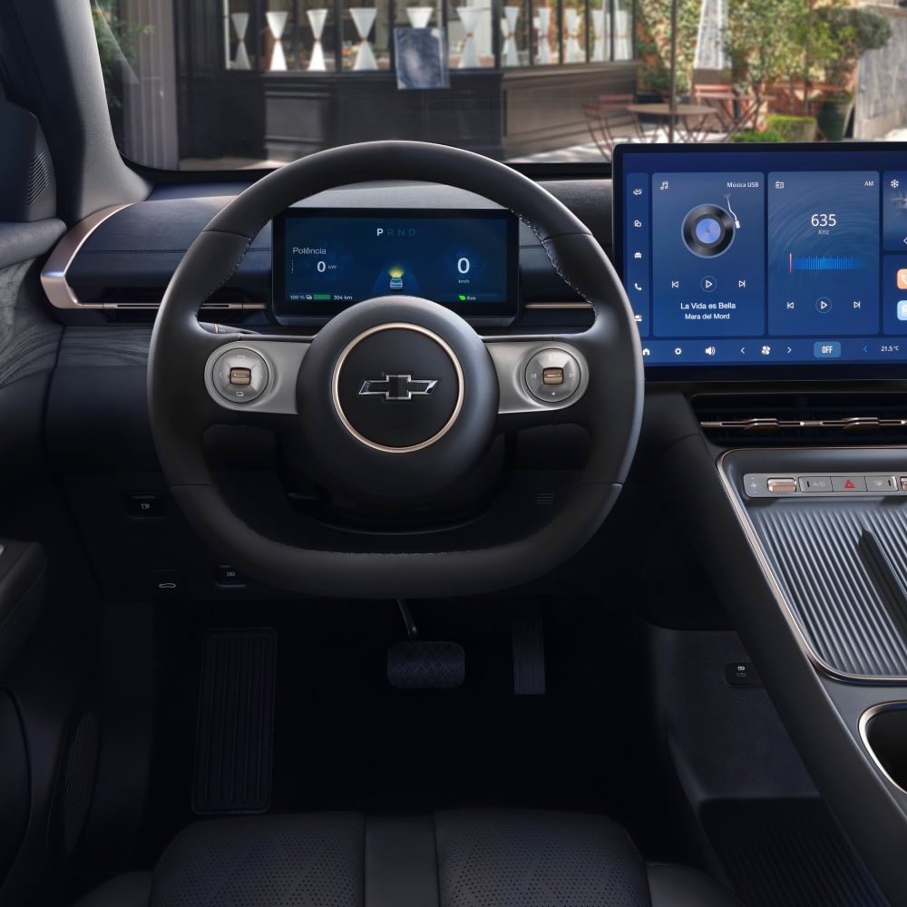 Interior do SUV Chevrolet Captiva EV, mostrando o volante com o logotipo da Chevrolet e o painel digital com duas telas grandes de comando e entretenimento.