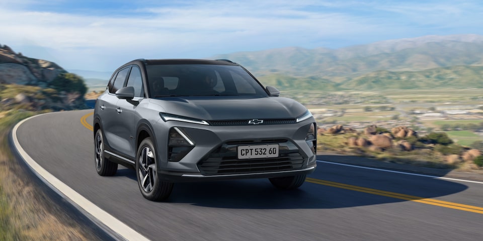 Chevrolet Captiva EV em movimento em uma estrada sinuosa cercada por montanhas e vegetação sob céu azul.