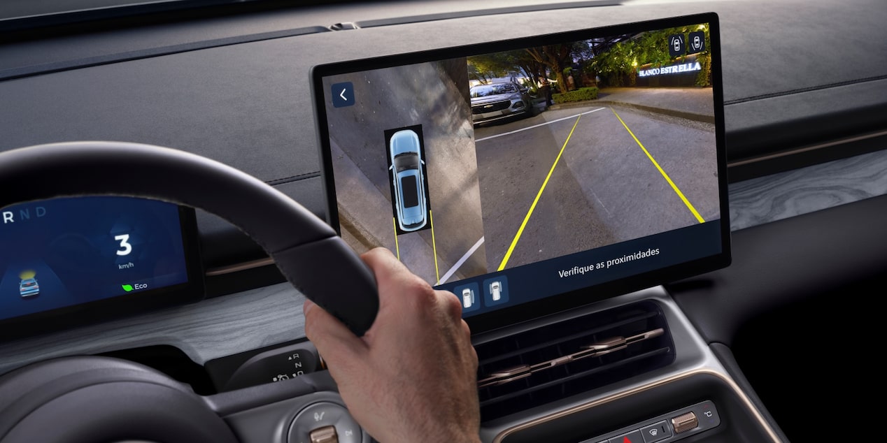 Condutor ao volante de um SUV Chevrolet Captiva EV, com a tela central exibindo o sistema de câmeras de ré e visão 360 graus para auxílio de estacionamento.