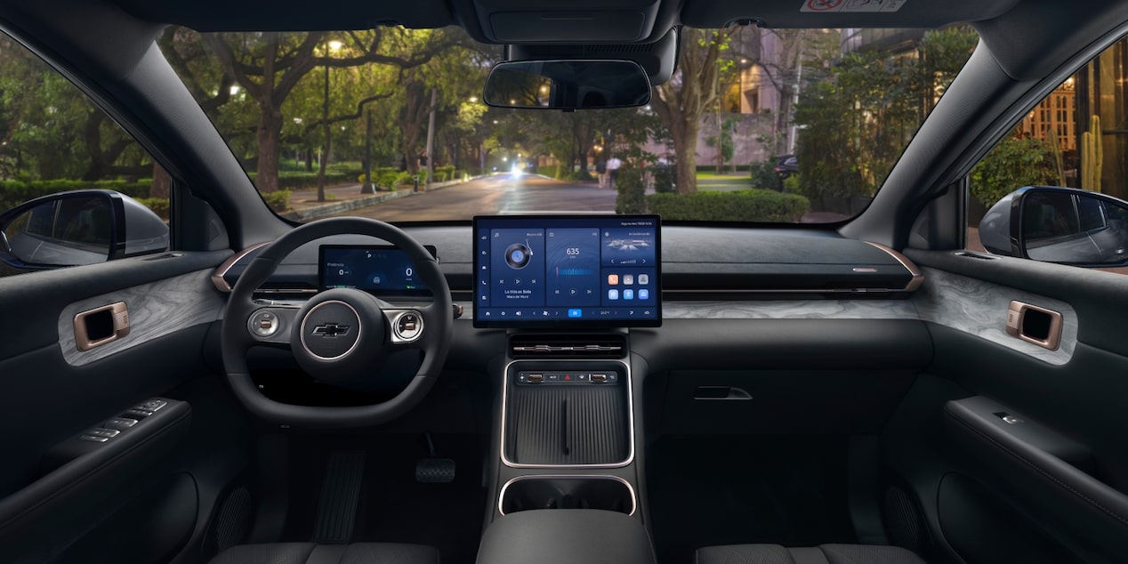 Interior do SUV Chevrolet Captiva EV visto do banco do motorista, com volante, painel digital e tela central acesa, mostrando rua arborizada através do para-brisa.