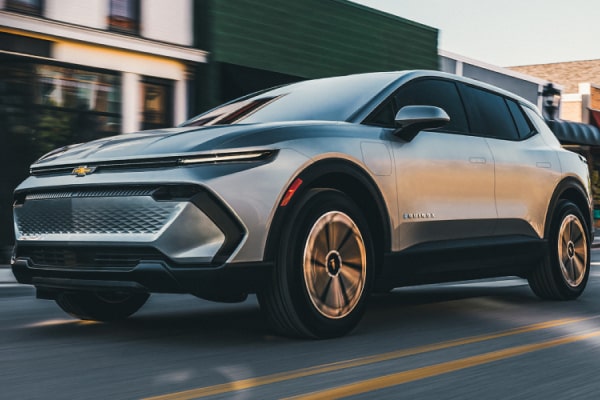 Chevrolet Equinox EV em foto ambientada. O SUV aparece em movimento, acelerando em uma rua diante de estabelecimentos comerciais.