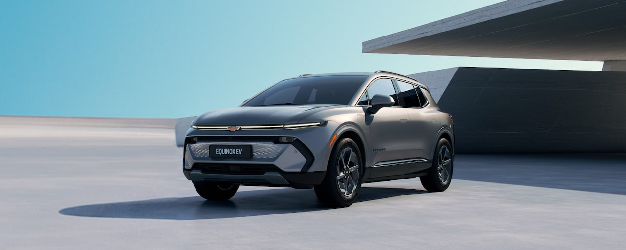 Equinox EV em imagem ambientada, estacionado diante de uma edificação com arquitetura assinada, fazendo com que as linhas do veículo sejam continuadas pelas linhas do prédio. No quadrante superior esquerdo, o texto: 2025 - Equinox EV; no quadrante inferior esquerdo, o preço sugerido: a partir de R$ 349.990; no quadrante inferior direito, os botões: faça um test drive e solicitar contato.