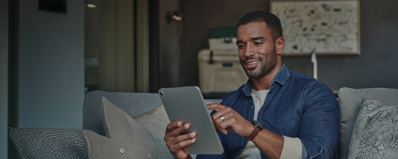 Homem negro sentado no sofá enquanto navega na internet usando um tablet e sorri de maneira simpática e cativante. No quadrante superior, o texto: General Motors Brasil - Política de privacidade e Lei Geral de Proteção de Dados Pessoais