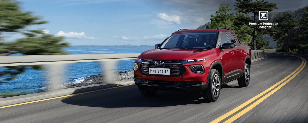 Montana RS vermelha em movimento na estrada, ladeada pelo oceano. No canto superior direito, o selo GM – Premium Protection Blindagem.