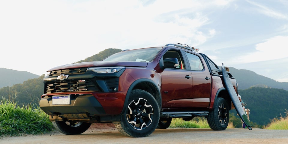 Chevrolet S10 Z71 2026 na cor vermelha, em ambiente ao ar livre com montanhas ao fundo. Um par de pranchas de surfe do influenciador Lucas Xaparral está apoiado na caçamba, destacando o perfil aventureiro e esportivo do modelo.