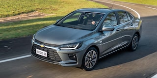 Chevrolet Onix Sedán circulando por una carretera rodeada de árboles.