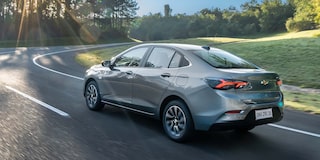 Chevrolet Onix Sedán circulando por una carretera rodeada de árboles, visto desde atrás.