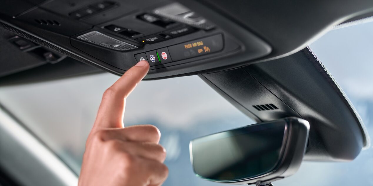 Imagen en primer plano de la mano de una persona activando el botón de OnStar desde su vehículo Chevrolet. 