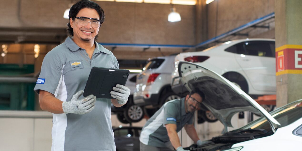 Imagen de dos mecánicos Chevrolet, uno de ellos sujetando una tablet y el otro revisando el motor de un vehículo.