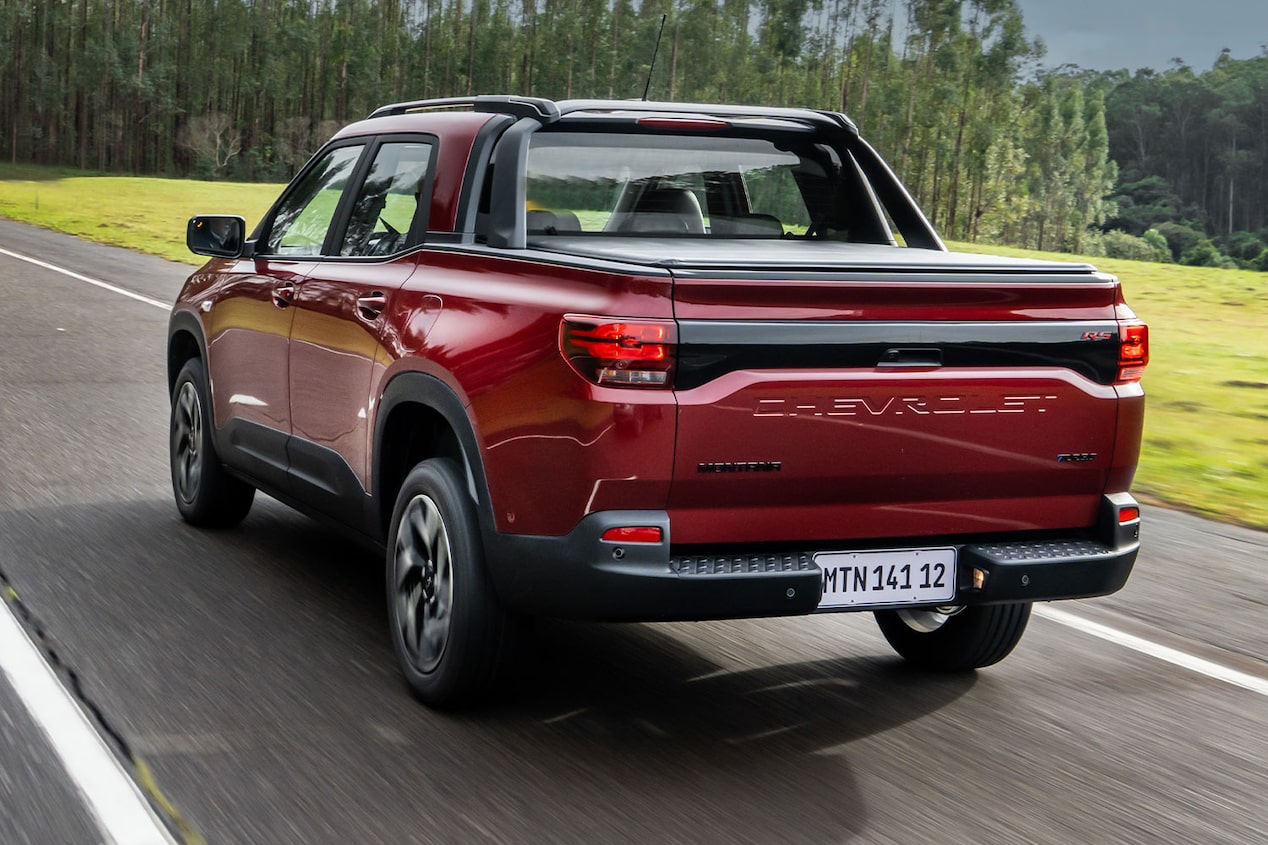 Vista trasera de una Chevrolet Montana Roja circulando por una carretera con vegetación de fondo.