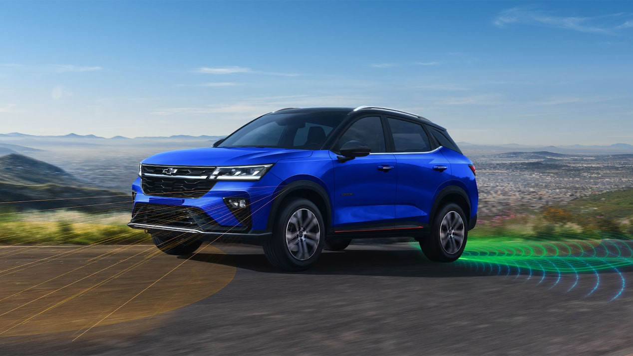 Chevrolet Groove en una carretera panorámica. En el lado izquierdo, se ven líneas naranjas simulando ondas que emanan de la parte delantera del vehículo, indicando detección frontal. En el lado derecho, líneas verdes simulando ondas emanan de la parte trasera del vehículo, indicando detección trasera. 