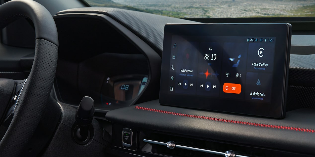 Pantalla táctil del sistema de infoentretenimiento de la Chevrolet Groove, con conectividad Apple CarPlay y Android Auto, mostrada junto al volante y detalles interiores con costuras rojas.
