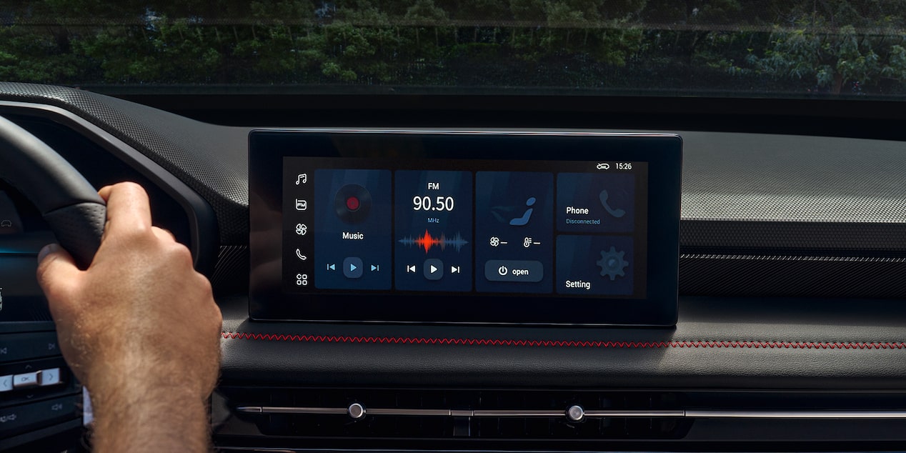 Pantalla central de la Chevrolet Groove mostrando el sistema multimedia con radio FM, conectividad telefónica y menú de configuración, junto a detalles del tablero con costuras rojas.